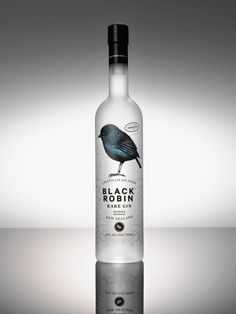 a bottle of black rock gin on a reflective surface with a bird sitting on it