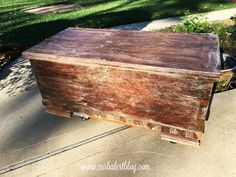 an old wooden box is sitting on the sidewalk in front of some grass and trees