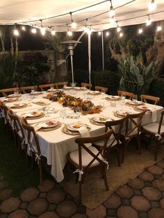 a table set up with plates and glasses for an outdoor dinner in the garden at night