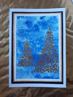 a blue and gold card with trees in the background on a sheet of metallic foil