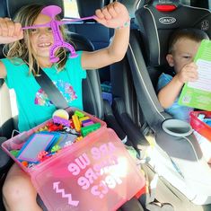 two young children sitting in the back seat of a car, one holding a toy