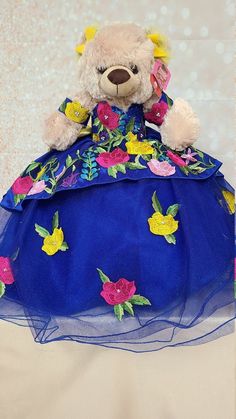 a teddy bear dressed in a blue dress with flowers on it's chest and head