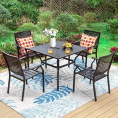 an outdoor dining table with four chairs and a rug on the ground in front of it