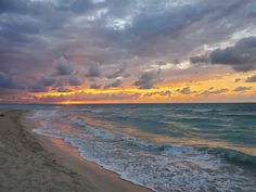 the sun is setting over the ocean with clouds in the sky and waves on the beach