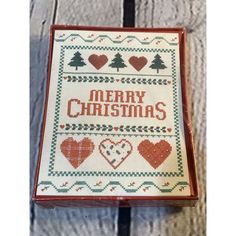 a cross - stitch christmas card with hearts and trees on it, in a wooden box