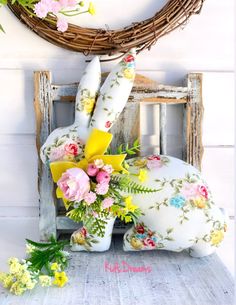 a bunny made out of flowers sitting in front of a wreath on a chair next to a wall