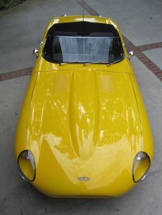 an old yellow sports car is parked on the street