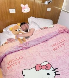 a man laying in bed with a hello kitty comforter and stuffed animal on his chest