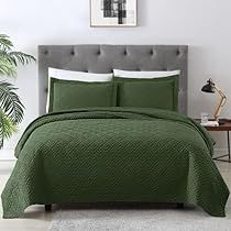 a bed with green bedspread and pillows in a white room next to a potted plant