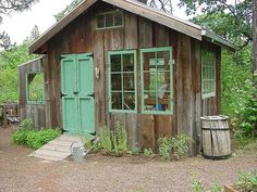 a small wooden building with green doors and windows in the woods next to a barrel