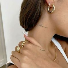 a woman with tattoos on her neck wearing gold hoop earrings and a white tank top