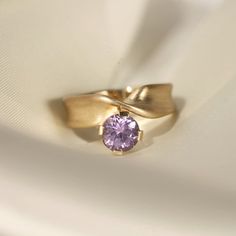 This one-of-a-kind stunner highlights a 1.45ct round sapphire with a mesmerizing purple hue. Crafted in 14k gold, the twisted band is inspired by a ribbon's flowy, satin-like movement. We love this ring worn solo for a subtle statement, or stacked for a mega look. Please note resizing this ring adds an extra 7-10 days for delivery. Elegant Purple Sapphire Solitaire Ring, Elegant Purple Solitaire Sapphire Ring, Elegant Pink Sapphire Round Band Ring, Elegant Pink Sapphire Birthstone Ring With Round Cut, Elegant Pink Sapphire Solitaire Ring, Elegant Round Amethyst Ring With Tension Setting, Purple Sapphire Ring, Classic Jewelry Pieces, Round Sapphire