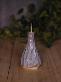 a small ceramic vase sitting on top of a wooden table next to a plant in the background