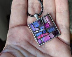 a hand holding a square pendant with colorful tiles on it's back and inside