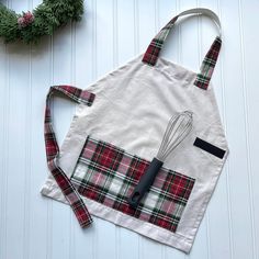 an apron with a whisk on it next to a wreath and utensils