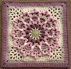 a crocheted square with pink and white flowers on the center, sitting on carpet