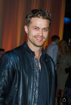 a man in a leather jacket smiling at the camera