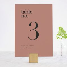 a pink table number card with the number three printed on it and a plant in a vase