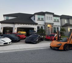 a group of exotic cars parked in front of a house with two garage doors open