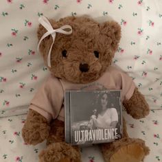 a brown teddy bear with a book on it's lap sitting on a bed