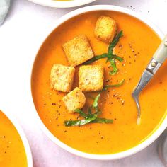 two bowls of soup with croutons and garnishes on the side