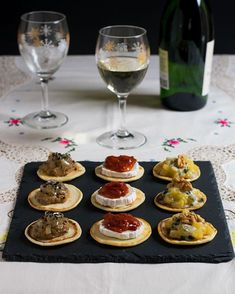 there are many appetizers on the table ready to be eaten with wine in the background