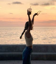 a woman standing on top of a sidewalk next to the ocean holding a plastic bucket