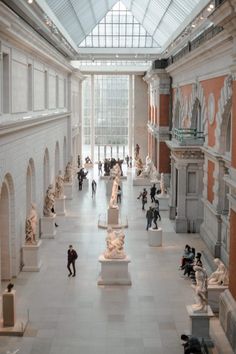 many people are walking around in a large room with statues on the walls and ceilings