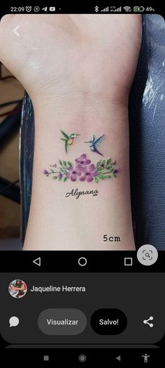 a small tattoo with flowers on the wrist and hummings flying above it, which reads