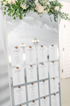 a wedding seating chart with flowers and greenery hanging from the wall in front of it