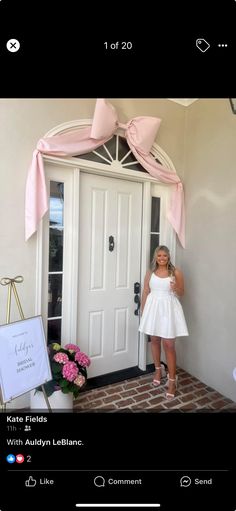 a woman standing in front of a door wearing a white dress and pink bow tie