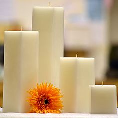 three tall candles with one orange flower on top and the other white in between them