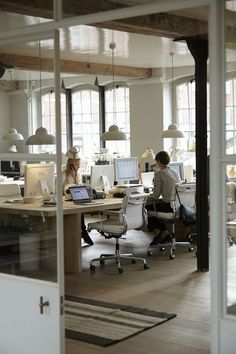 two people sitting at desks in an office with open laptops and desktop computers