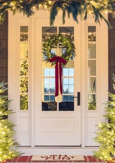 a christmas wreath on the front door of a house decorated with lights and garlands