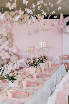 a table set up for a baby shower party with pink and white decorations hanging from the ceiling