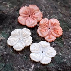 three pink and white flower buttons sitting on top of a stone slab next to a rock