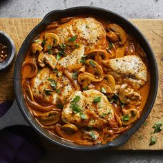 a skillet filled with chicken and mushrooms on top of a wooden cutting board