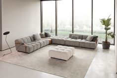 a modern living room with large windows and a sectional sofa in the middle, along with a footstool