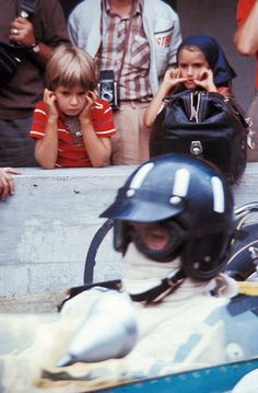 a young boy sitting in the back of a race car while holding onto a helmet