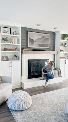 a woman sitting on the edge of a fireplace in a living room with white furniture