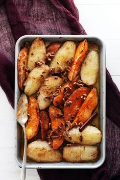 a pan filled with potatoes and nuts on top of a purple cloth next to a spoon