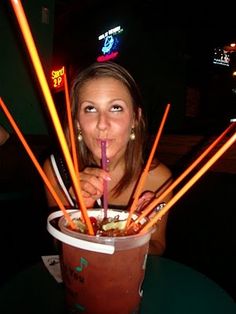 a woman sitting at a table with a drink in her hand and straws sticking out of it