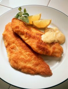 two fish fillets on a white plate with lemon wedges