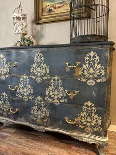 an old blue dresser with gold paint on it and a birdcage in the background