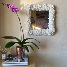 a flower in a vase sitting on top of a table next to a book and mirror