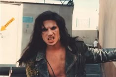 a man with long hair and piercings on his face is standing in front of a building