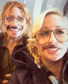 two women with fake moustaches on their faces posing for a selfie