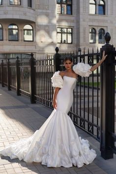 a woman in a white wedding dress leaning on a black fence with her arms outstretched