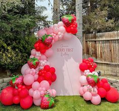 a bunch of balloons and some strawberries on the ground in front of a grave