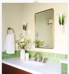 a bathroom with green and white tile on the walls, sink and mirror above it